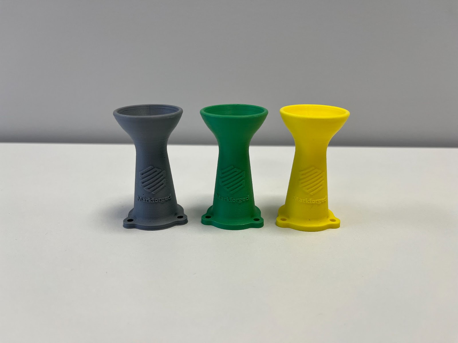 three markforged 3d printed parts in different colours, each featuring the markforged logo