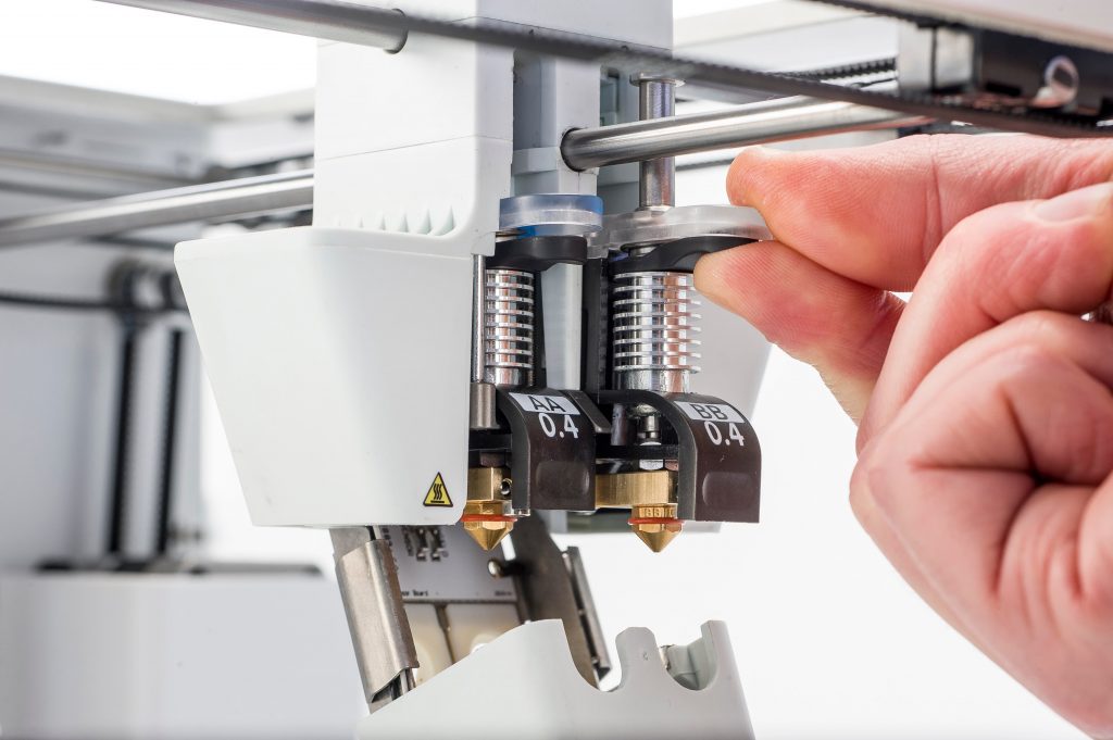a hand reaching in to adjust the print core of a 3D printer