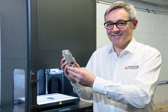 an "angus 3d solutions" employee holds a 3d printed metal part, with the markforged machine that printed it in the background