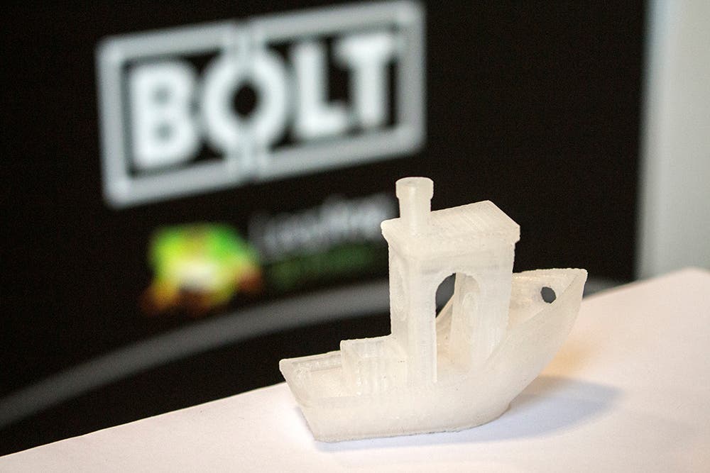 a 3d printed benchy (benchmark print design) stood in front of a "Bolt by leapfrog" logo