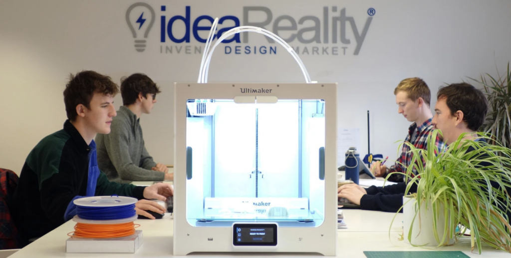 four men work on laptops, an ultimaker 3d printer stands in the centre