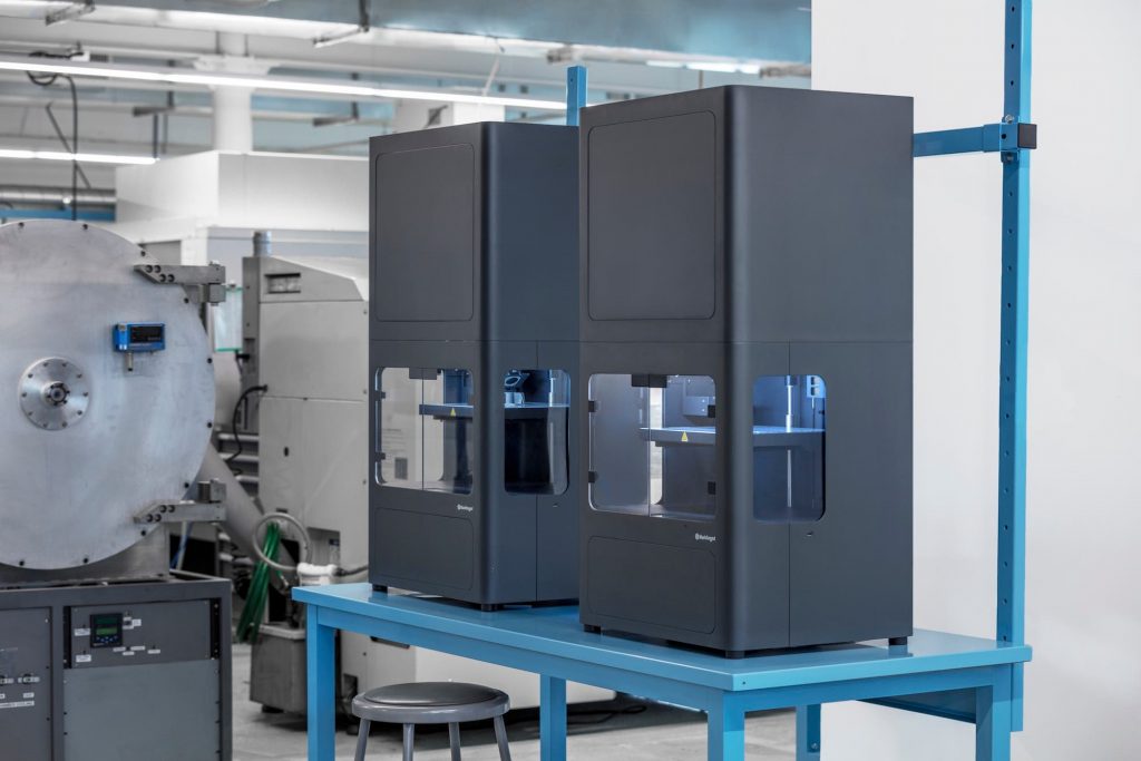 two large markforged metal X printers stand beside each other on a desktop in a factory