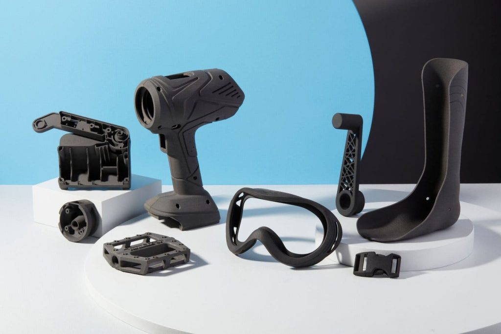 A selection of 3d printed parts Nylon-11 - including a bicycle crank shaft, bike pedal, electrical drill housing, belt buckle, and goggles (without the lens)