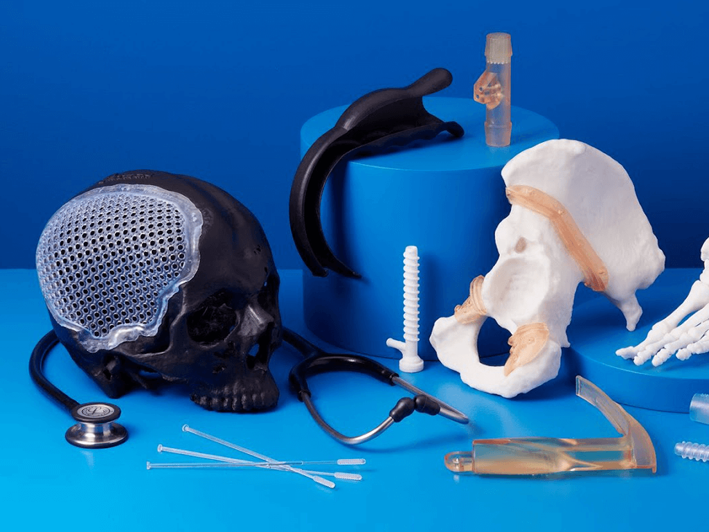 an assortment of 3d printed medical related devices, including part of a skull, a hip bone, surgical implements, and a nasal swab device