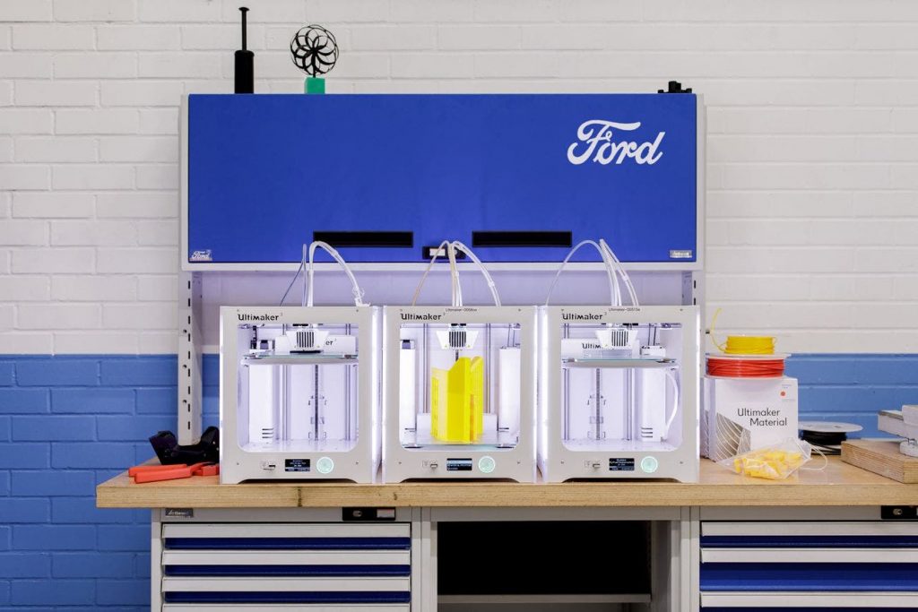 three ultimaker 3d printers sat on a desktop in front of a large Ford logo