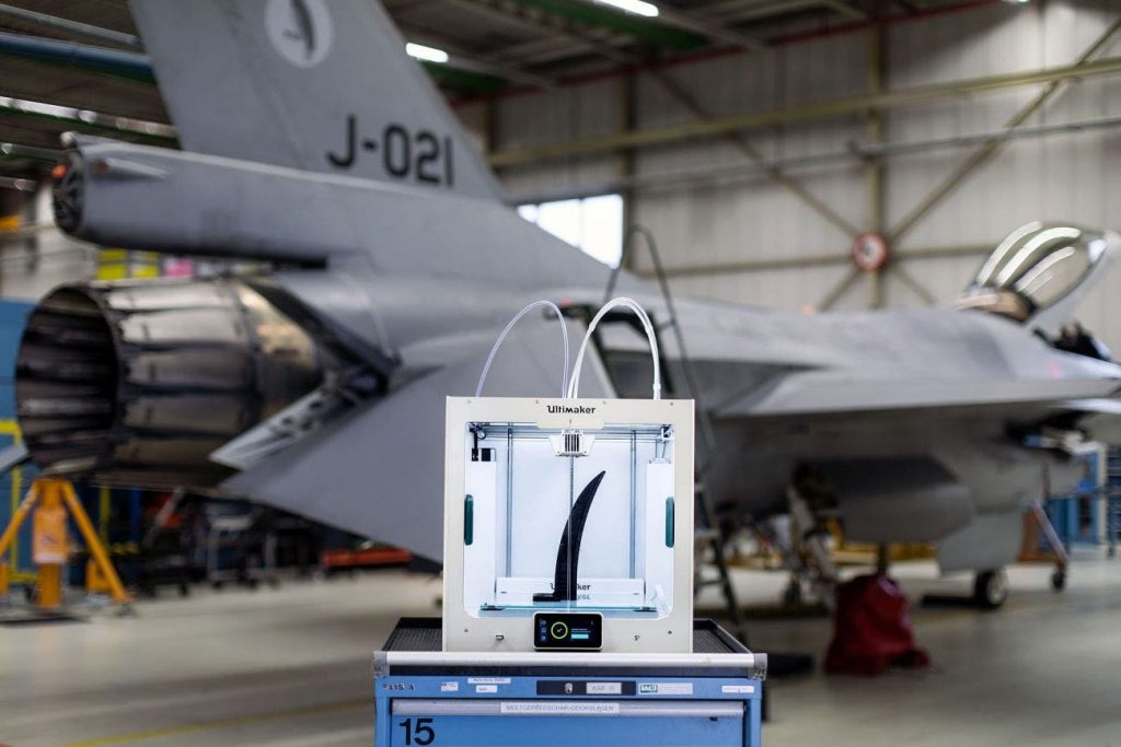 an ultimaker s5 3d printer stood in front of a large fighter jet in a hangar