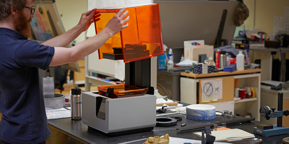 a man opens up a form 2 3d printer by formlabs to inspect the build area