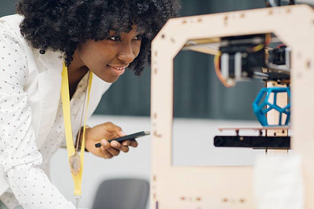 A woman using a 3D printer and monitoring it with her phone