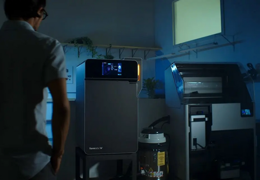 A man looking on at a formlabs fuse 1 printer in a modern, blue lit room