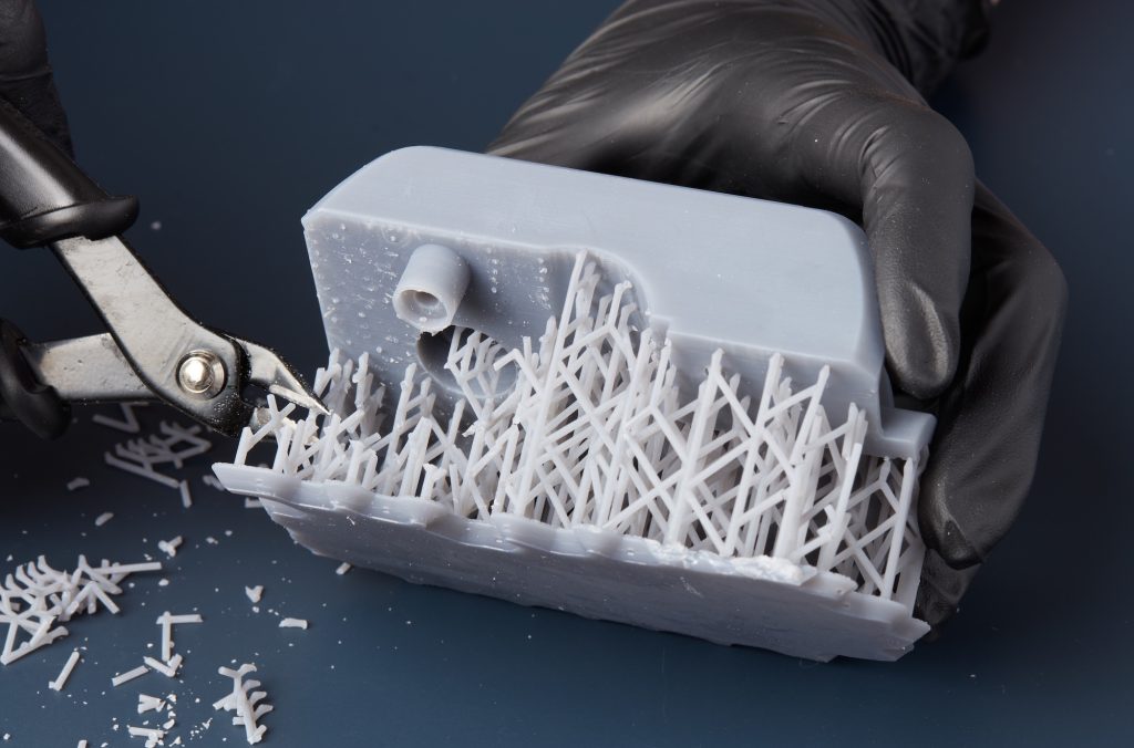 A person removing the supports from a resin printed part using pliers.