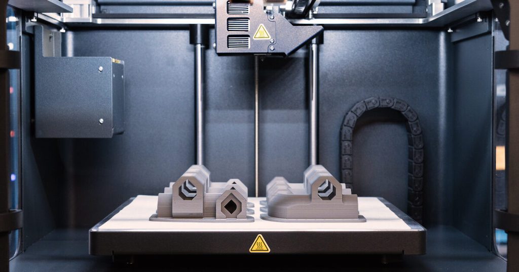 A Markforged Metal X 3D printer with multiple metal parts sat on the print bed.