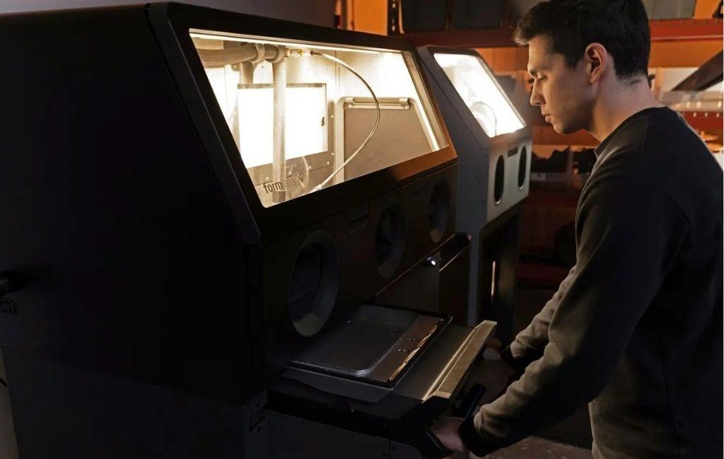Operator using the Formlabs Fuse Sift X1 powder recovery station to depowder SLS parts